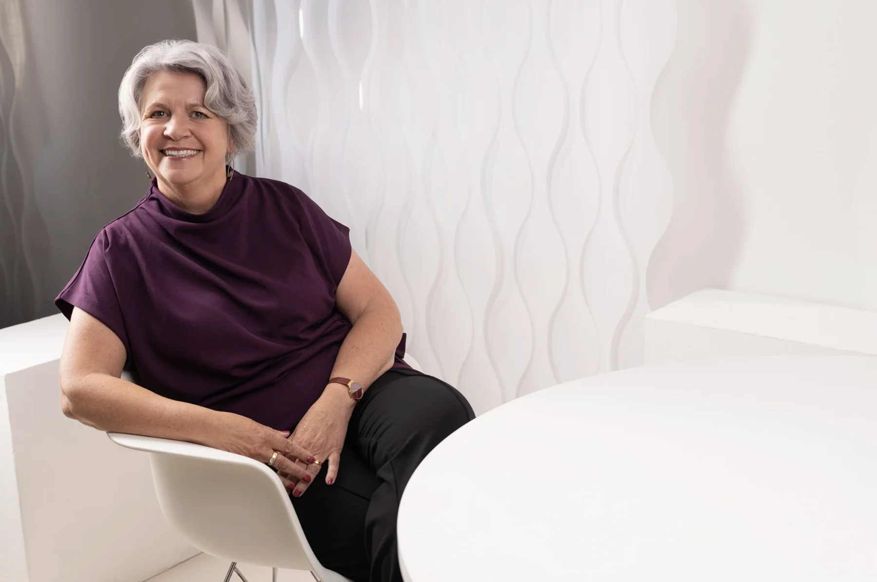 Team-Fotografie für Unternehmen: Mitarbeiterin im aubergine Oberteil am weißen Tisch – einheitlicher Look Team-Porträt: Mitarbeiterin im aubergine Oberteil am weißen Tisch – einheitliche Bildsprache, Business-Fotografie Cristina Galler